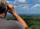 man with binoculars looking out on forest canopy 